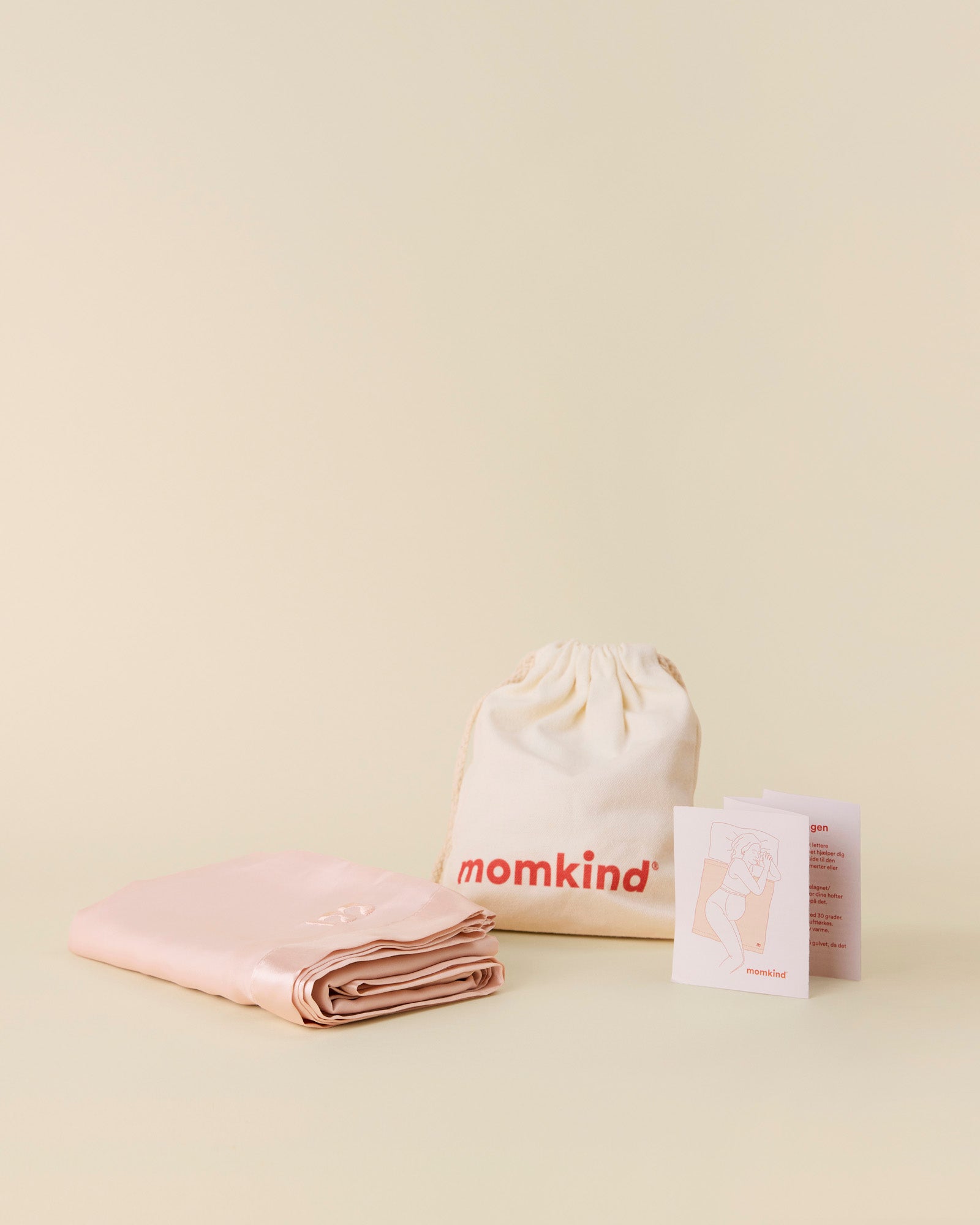 Momkind glidelagen i lyserød med momkind logo på. Pose til momkind glidelagen og brugsanvisning.