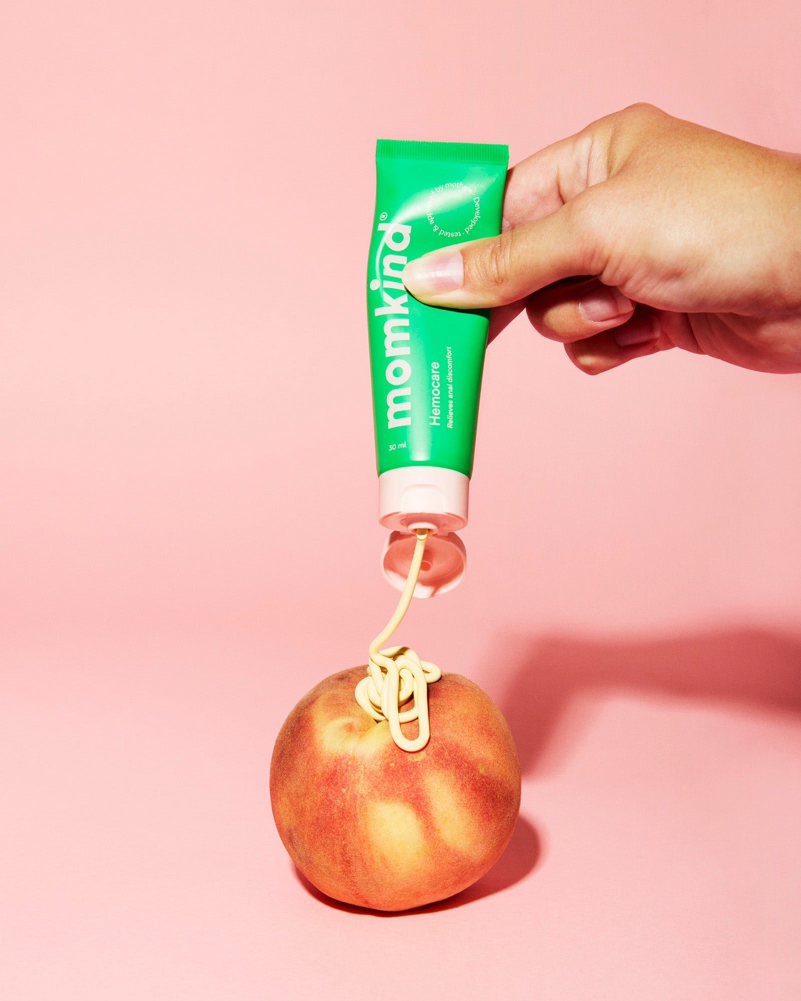 hæmoridecreme klemmes af en hånd, så det sprøjtes ud over en fersken