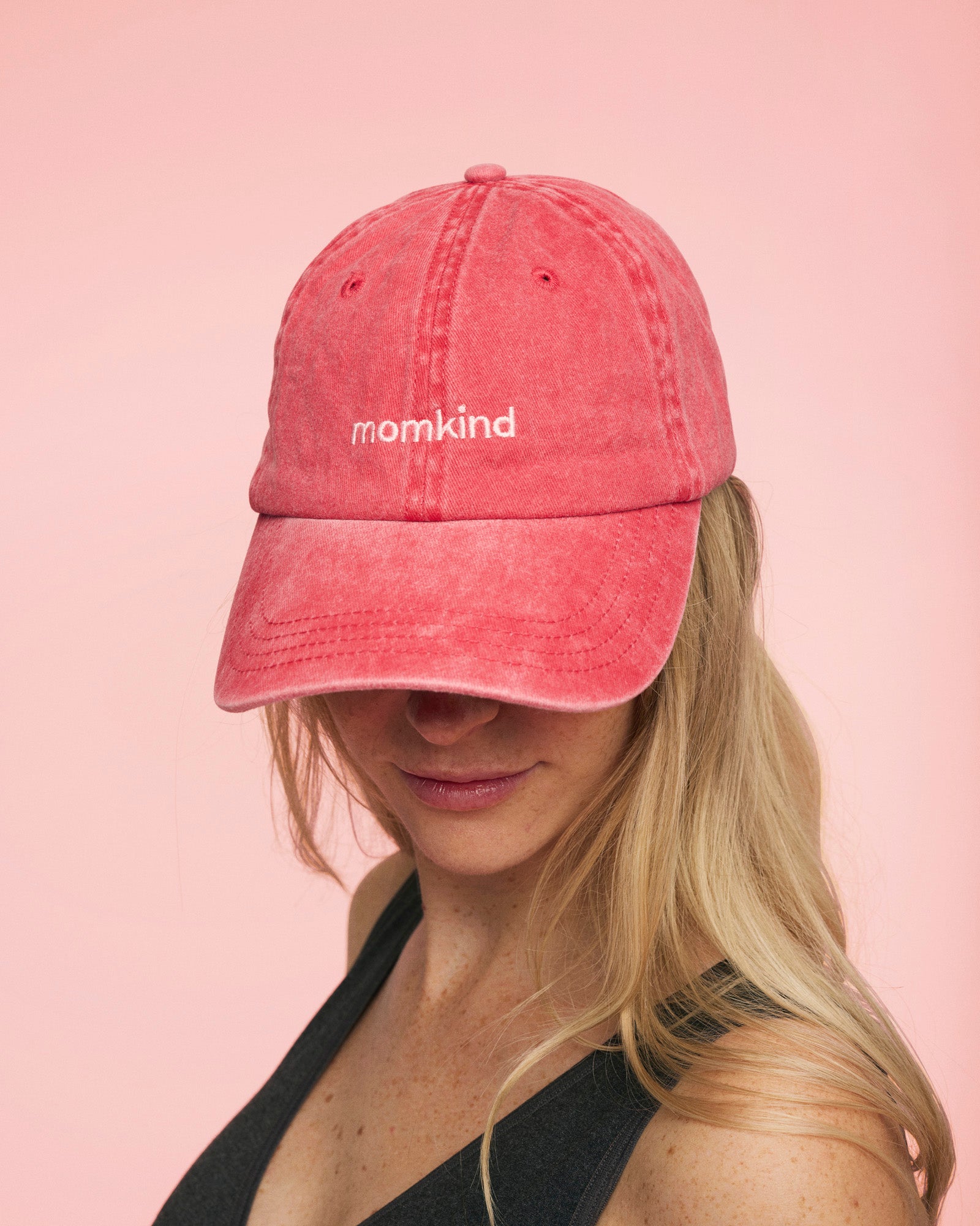 Momkind cap I roed med lyseroed logo. Den sidder på kvindes hovede som kigger ned.