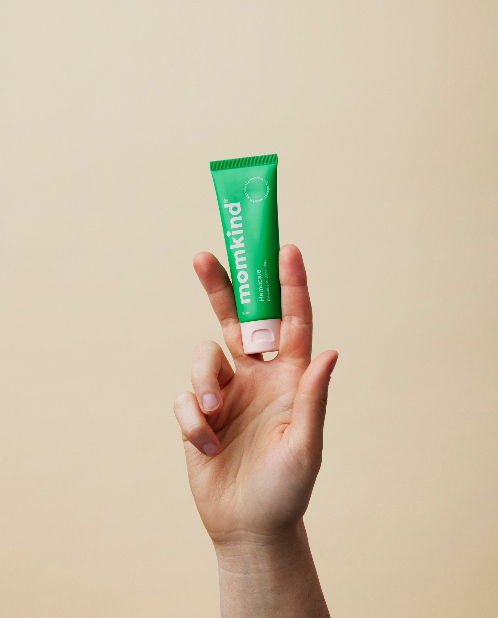 hånd der holder momkind hæmoridecreme op mellem pegefinger og langefinger