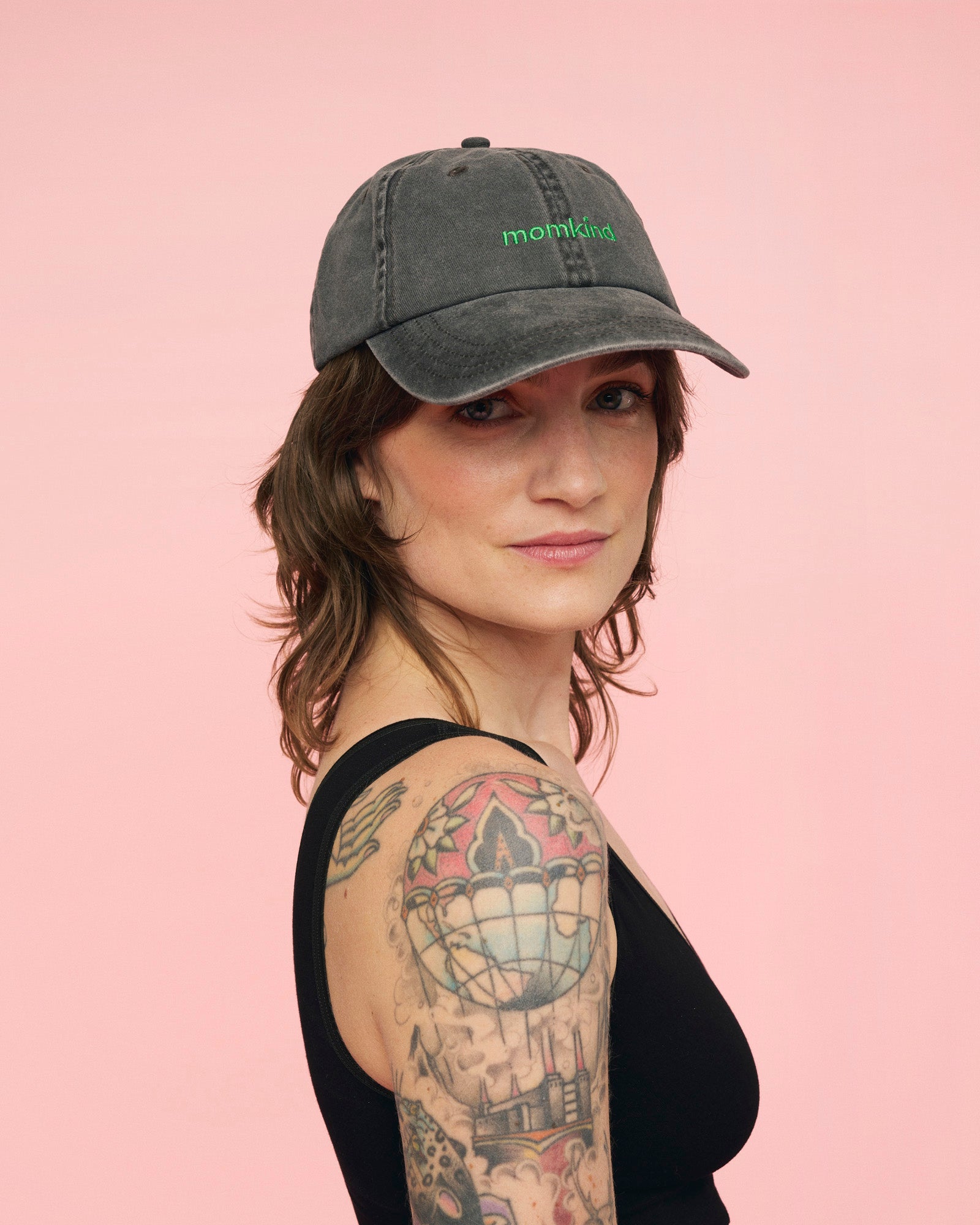 Momkind cap I sort med groent logo. Den sidder på hovedet af en kvinde, hvor den kan ses forfra.