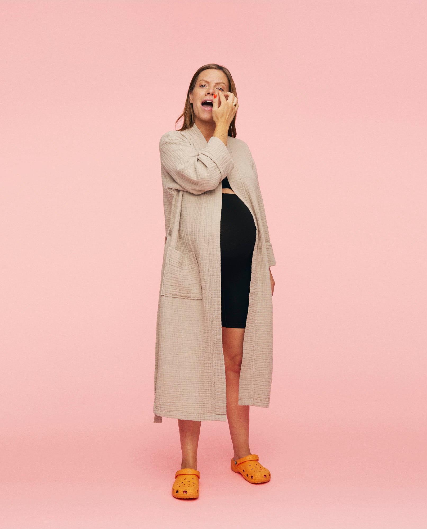 Kvinde iført momkind morgenkåbe. Kåben er åben, hun klør sig på næsten mens hendes gravide mave stikker ud af kåben.