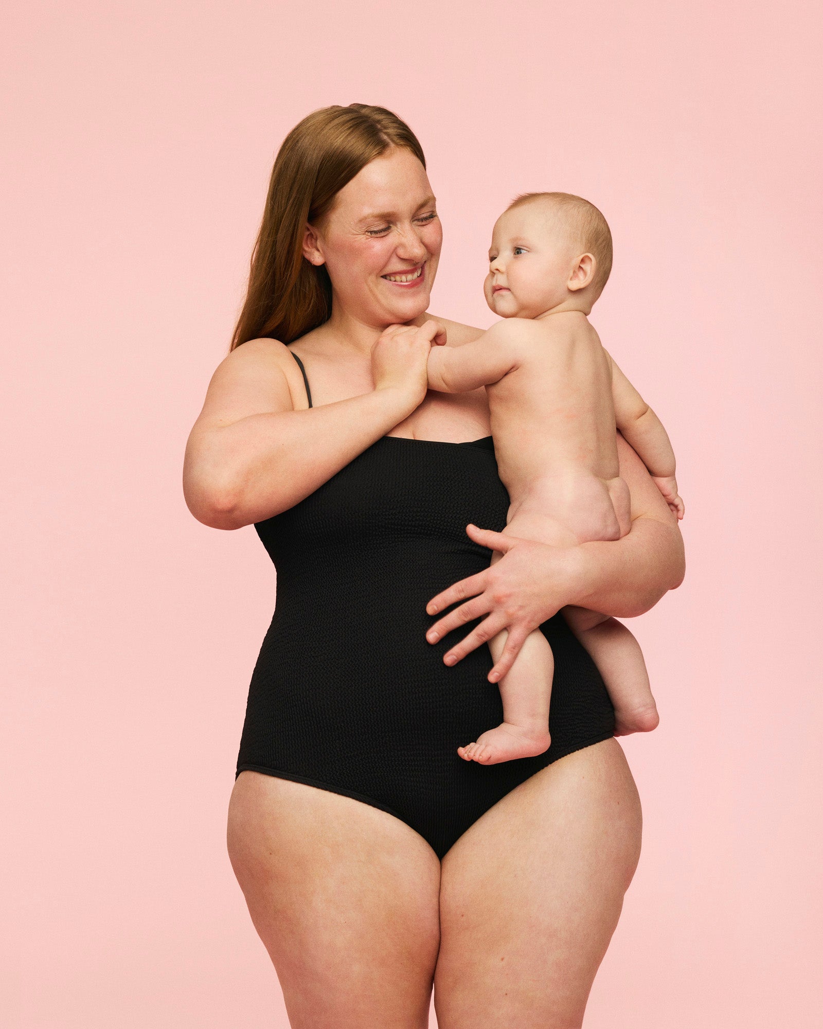 Kvinde som bærer sit barn iført momkind gravid badedragt i farven sort.