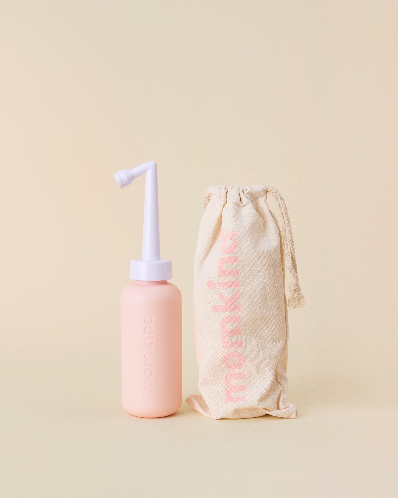 post partum skylleflaske i lyserød står ved siden af tilhørende pose fra momkind