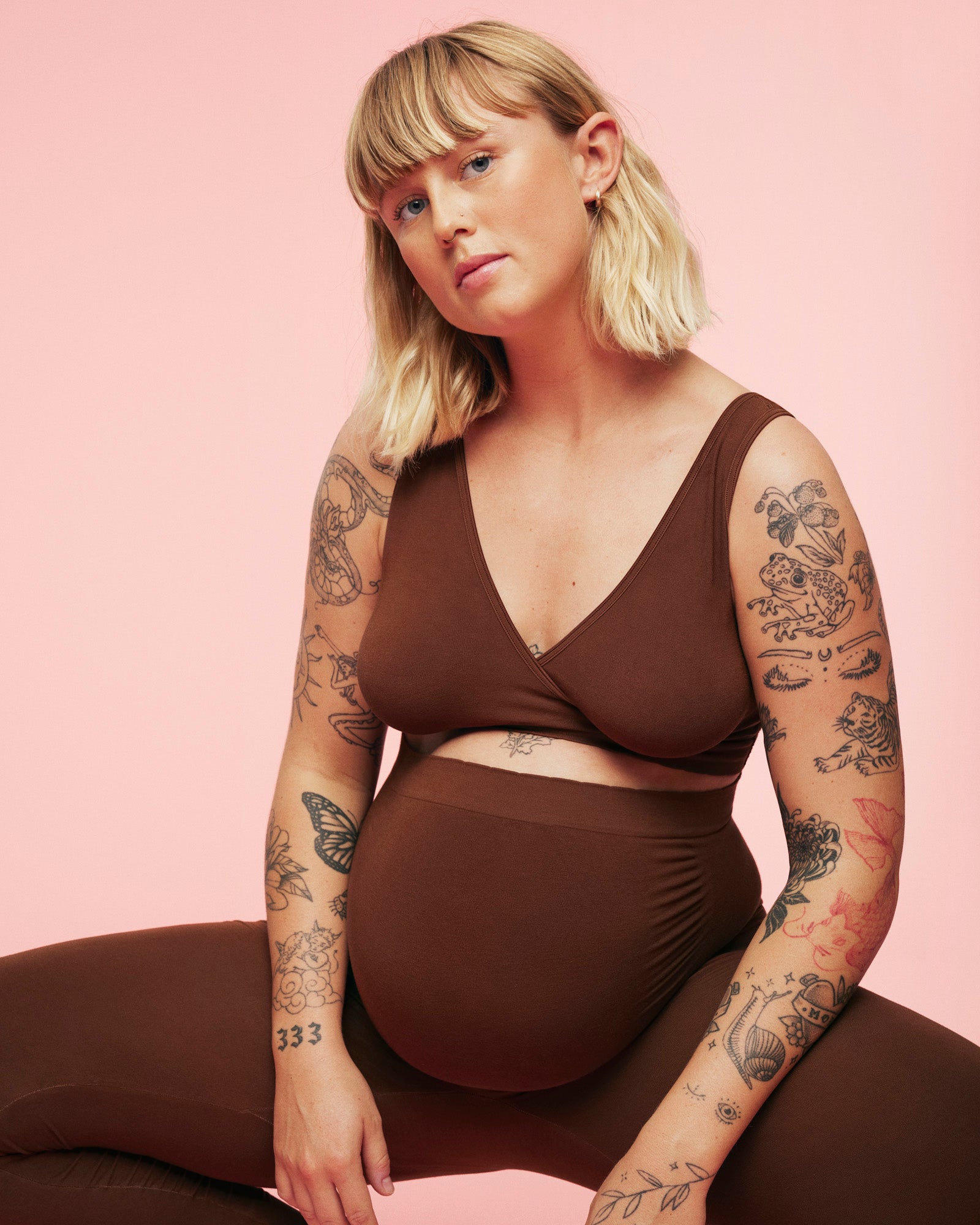 Gravid kvinde sidder på hug imens hun er iført momkind gravid leggings og amme bh. Man kan se der er godt med stræk i leggings på den måde hun sidder. 