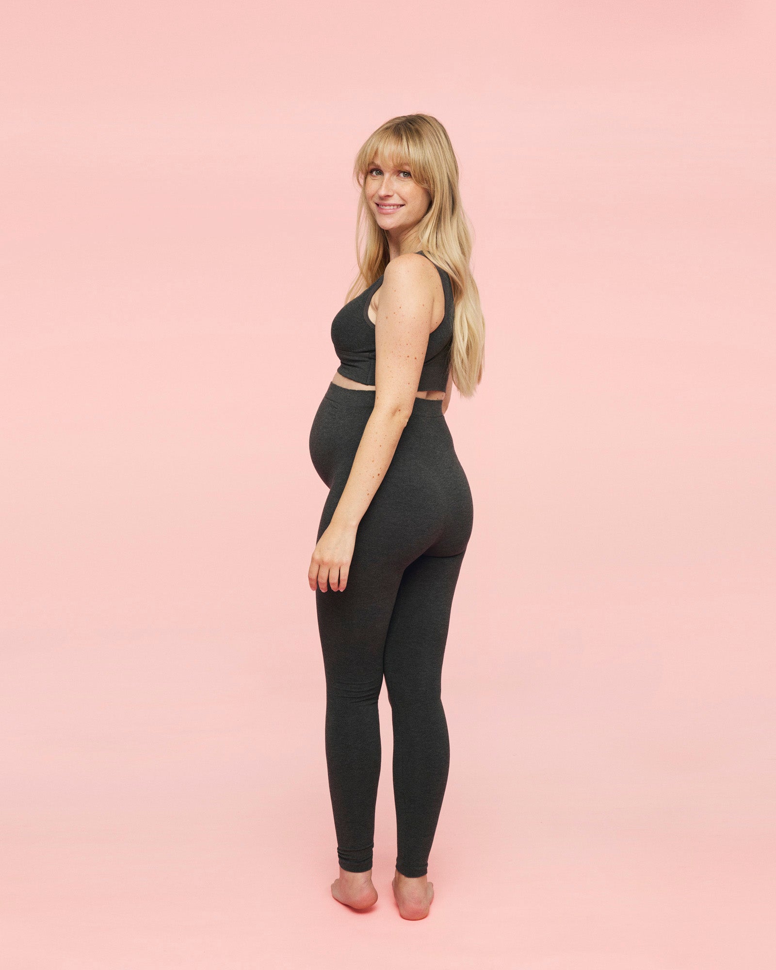 gravid kvinde står med ryggen til iført momkind gravidleggings i grå og crossover amme bh i grå fra momkind