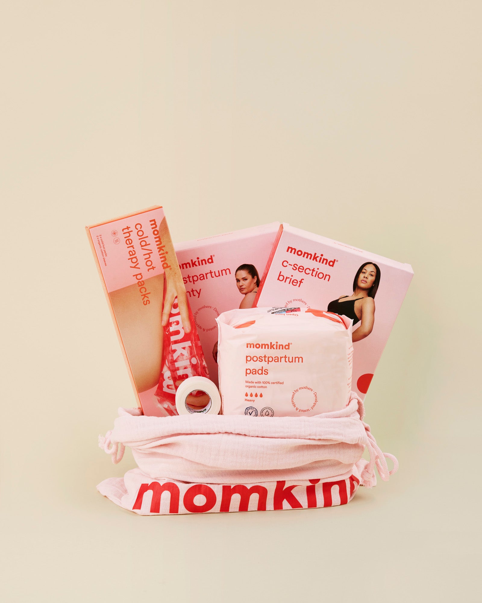 Momkind mellem efterfoedselspakke til kejsersnit. Posen indeholder englehud plaster, efterfoedselsbind, efterfoedselstrusser, kejsersnittrusser og koele/varme pose.