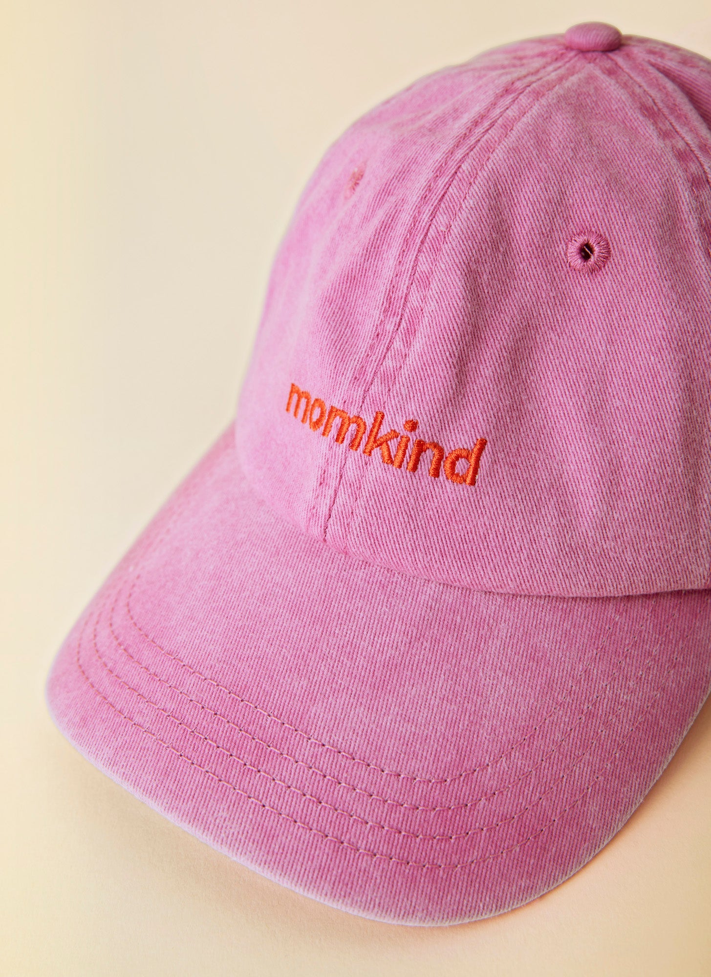 Momkind cap I lyseroed og roed logo. Kasket ses helt tæt på fra fronten.