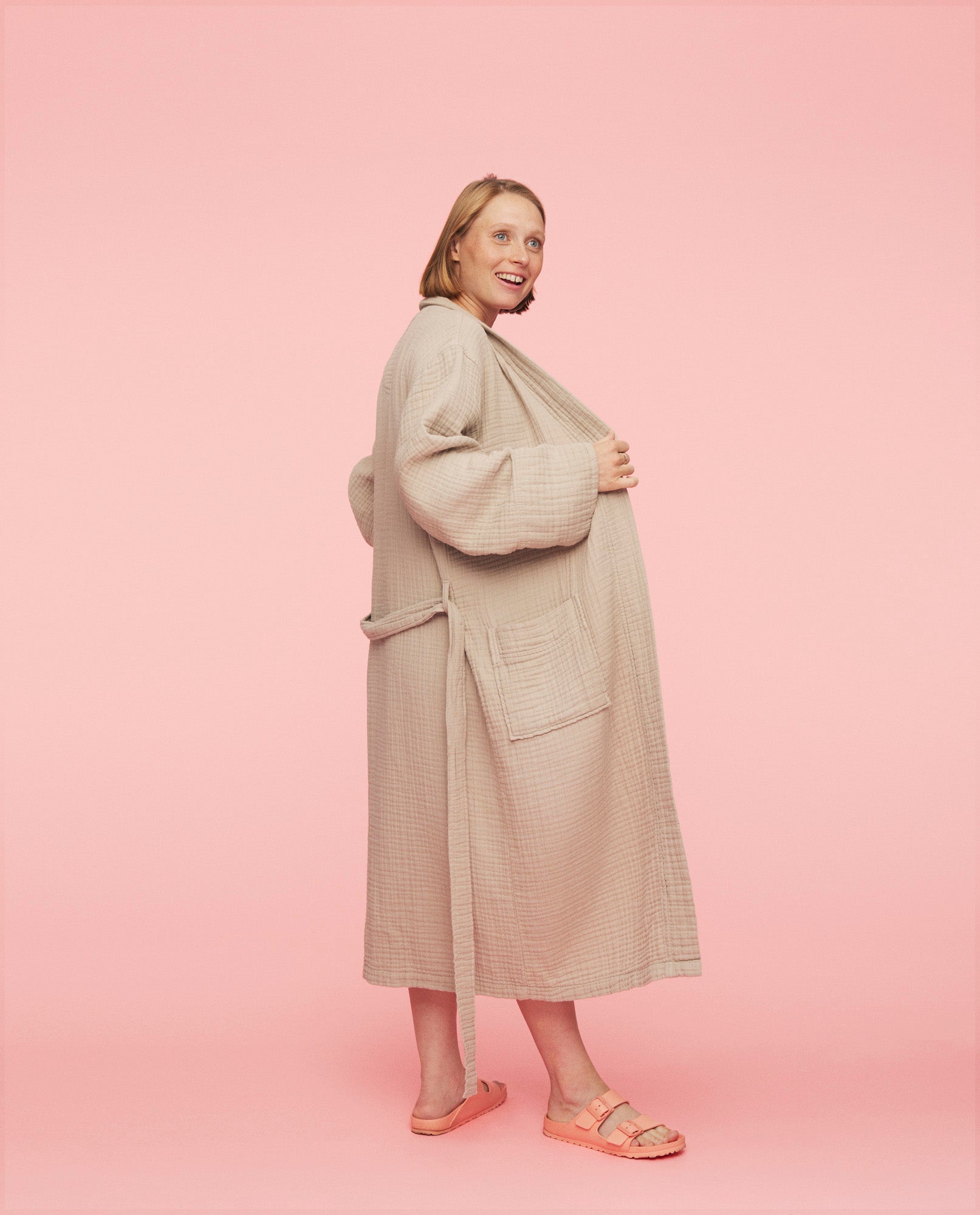Kvinde har the kind robe på fra momkind i beige. Hun står fra siden og er ved at lukke kåben.