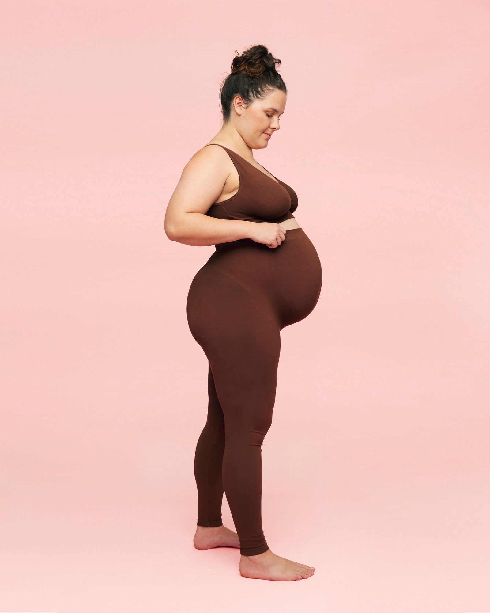 gravid kvinde kigger ned på sin mave iført brune leggings til gravide fra momkind og crossover ammebh i brun fra momkind