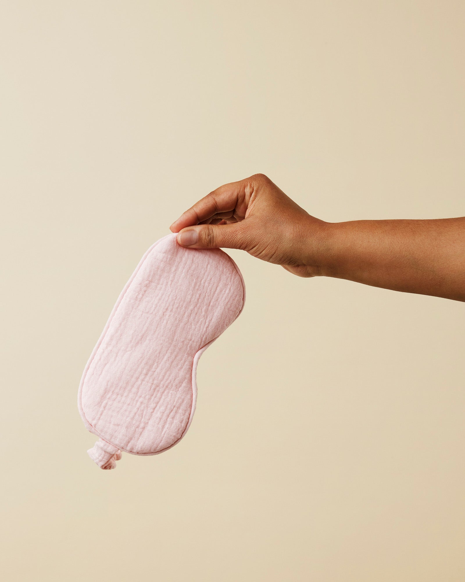 Momkind sovemaske I organic cotton I farven lyseroed. En hånd holder sovemasken i luften.