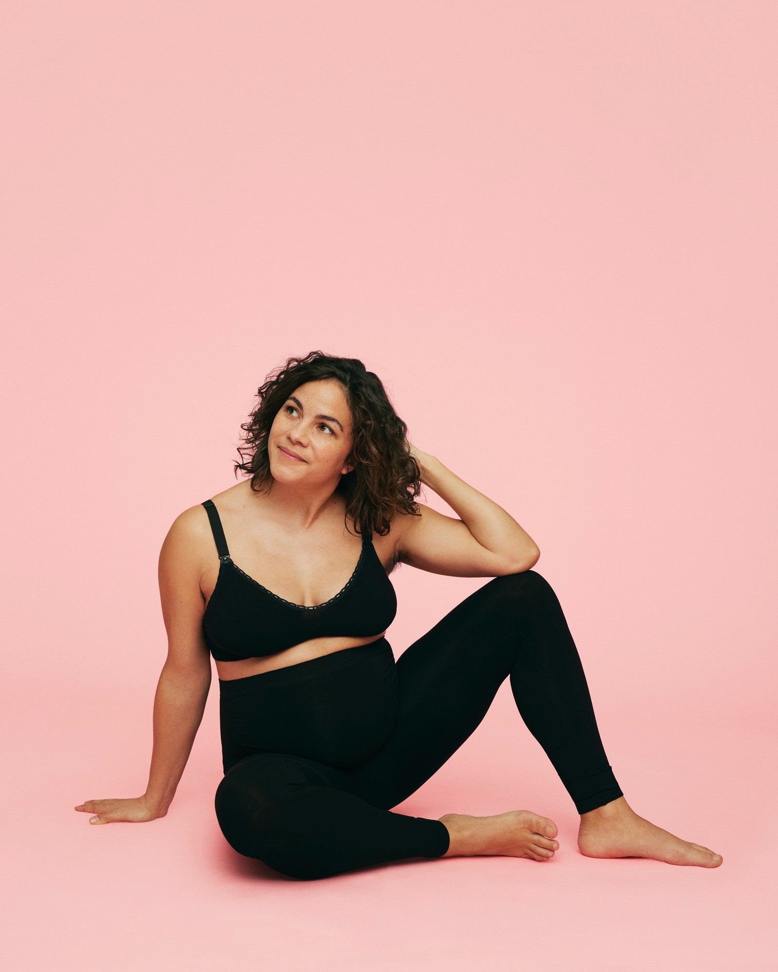 gravid kvinde sidder på gulvet med den ene hånd i håret iført sorte leggings til gravide fra momkind og blød ammebh uden bøjle i sort fra momkind